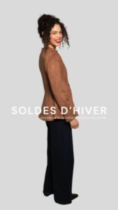 Femme souriante portant une veste en suède marron et un pantalon noir, posant de profil.