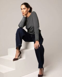 Femme assise sur des marches, portant un pull gris et un pantalon bleu marine, avec des escarpins marron.