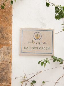Plaque murale indiquant 'DAR BEN GACEM' avec des motifs décoratifs sur un mur blanc.