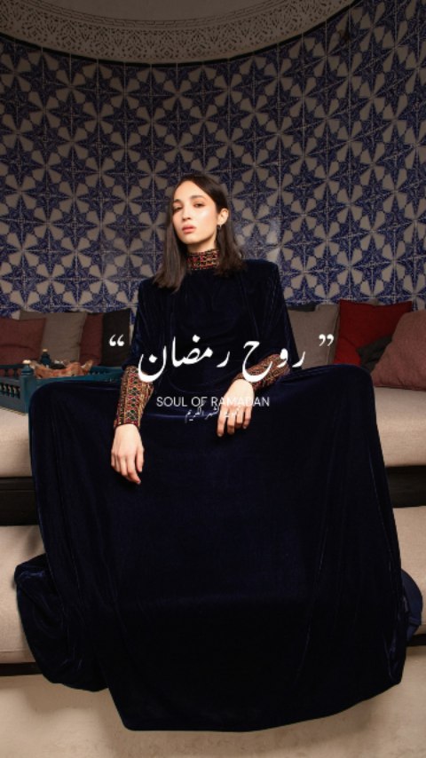 Femme portant une robe longue noire avec des motifs colorés sur les manches, assise dans un environnement décoratif.