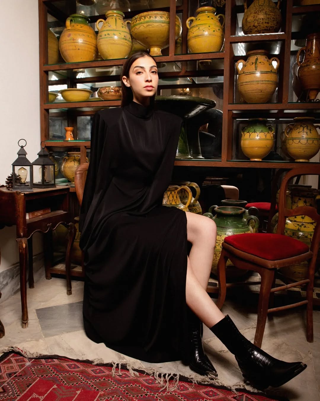 Femme en robe noire assise sur une chaise, avec des pots en céramique jaune en arrière-plan.