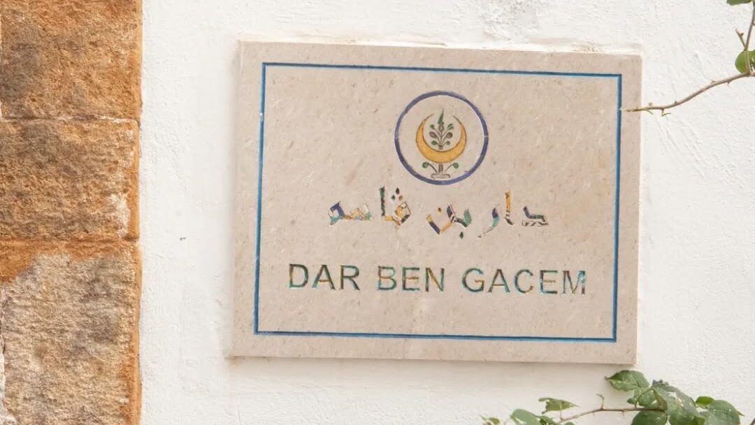 Plaque murale indiquant 'DAR BEN GACEM' avec des motifs décoratifs sur un mur blanc.